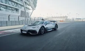 Srebrny Mercedes-AMG Project One pędzi po torze wyścigowym, obok nowoczesnej architektury.