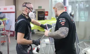 Dwóch mężczyzn w maskach i rękawiczkach pracuje nad zielonym elementem, sprawdzając, czy na podkład epoksydowy można kłaść lakier.