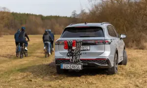 Srebrny SUV z rowerami na bagażniku i dodatkową tablicą rejestracyjną LU-246SL. W tle cztery osoby na rowerach.