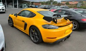 Żółty Porsche GT4 RS z dużym spojlerem, gotowy do wyścigów samochodowych, zaparkowany obok czarnych aut.