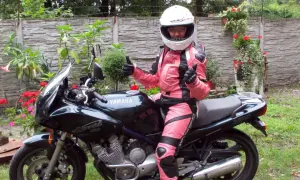 Niska dziewczyna w różowym kombinezonie motocyklowym i kasku siedzi na czarnym motocyklu Yamaha Diversion.