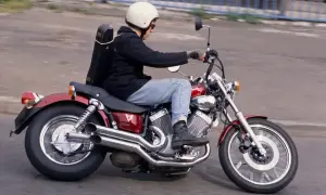 Motocyklista w kasku jedzie na czerwonym motocyklu Yamaha Virago, z futerałem na instrument muzyczny przypiętym z tyłu.