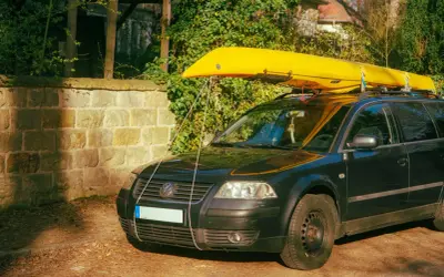 Żółty kajak na dachu czarnego kombi. Pokazuje, co można przewozić na dachu samochodu, np. sprzęt wodny.