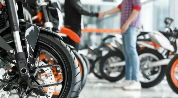 Zbliżenie na koło motocykla pcc-3 wzór. W tle dwóch mężczyzn ściska sobie dłonie na tle innych motocykli.