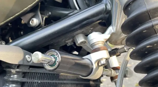 Amortyzator skrętu motocykl, zamontowany obok chłodnicy, zapewnia stabilność kierownicy podczas jazdy.