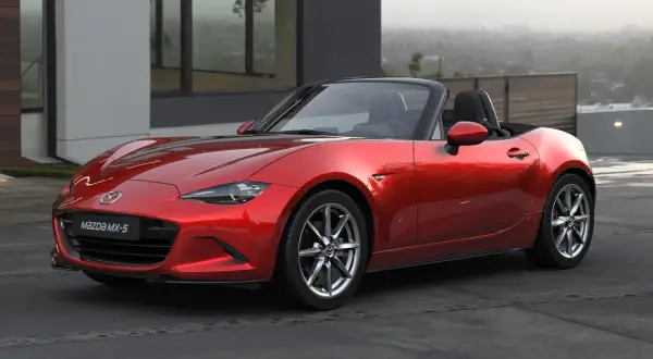 Czerwone Mazda MX-5, jedne z najbardziej pożądanych aut sportowych, lśni na tle nowoczesnej architektury.
