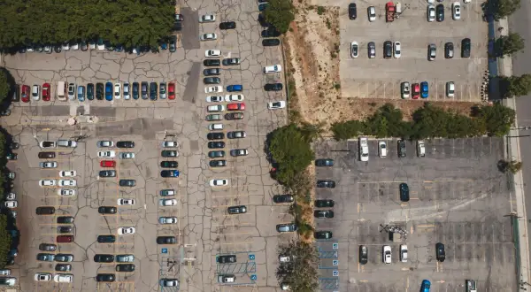 Widok z lotu ptaka na parking, gdzie doszło do kolizji na terenie prywatnym. Widać wiele zaparkowanych samochodów.