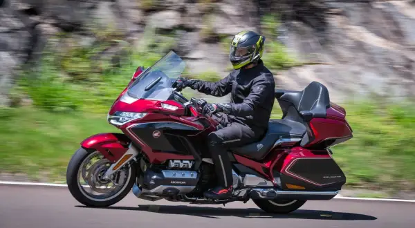 Mężczyzna w kasku jedzie lśniącym, czerwonym motocyklem do turystyki we dwoje. W tle rozmyty krajobraz.