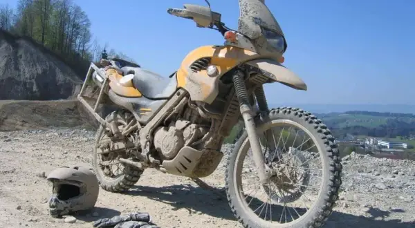 Żółty motocykl po off-roadowej przygodzie, pokryty błotem. Obok leżą kask i rękawice. Idealny do lekkiego enduro.