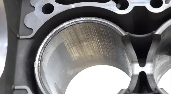 Zużyty cylinder w bloku silnika samochodu, z widocznymi śladami po tłoku.