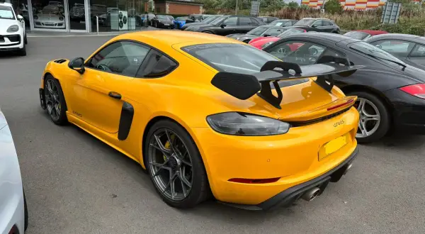 Żółty Porsche GT4 RS z dużym spojlerem, gotowy do wyścigów samochodowych, zaparkowany obok czarnych aut.