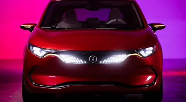 Czerwone izera auto z nowoczesnymi światłami LED i logo producenta na tle fioletowo-różowego oświetlenia.