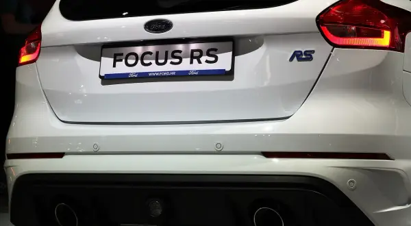 Biały Ford Focus RS z podwójnym wydechem i niebieskim znaczkiem RS.
