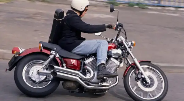 Motocyklista w kasku jedzie na czerwonym motocyklu Yamaha Virago, z futerałem na instrument muzyczny przypiętym z tyłu.