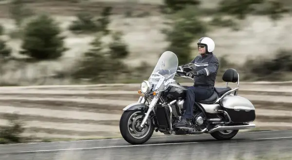 Mężczyzna w kasku jedzie na dużym motocyklu, który można nazwać chopperem. W tle rozmyty krajobraz.