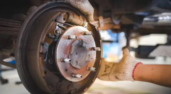 Mechanik w rękawiczkach wymienia elementy hamulcowe, w tym tarcza kotwiczna, w samochodzie.