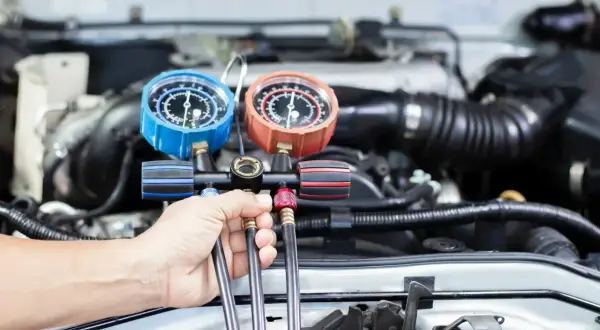 Mechanik wykonuje nabijanie klimatyzacji w samochodzie, używając manometrów do kontroli ciśnienia.