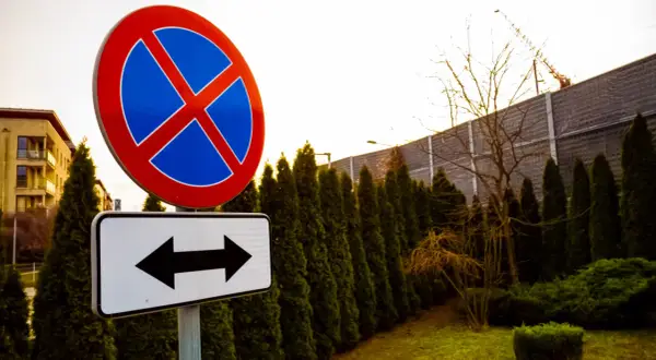 Znak zakazu zatrzymywania się i postoju, z tabliczką wskazującą kierunki. Uważaj, bo grozi za to mandat.