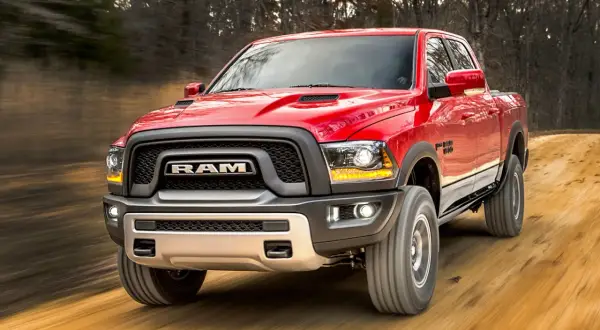 Czerwony Dodge Ram Rebel pędzi po leśnej drodze. Poznaj jego imponujące dodge ram wymiary i możliwości terenowe.