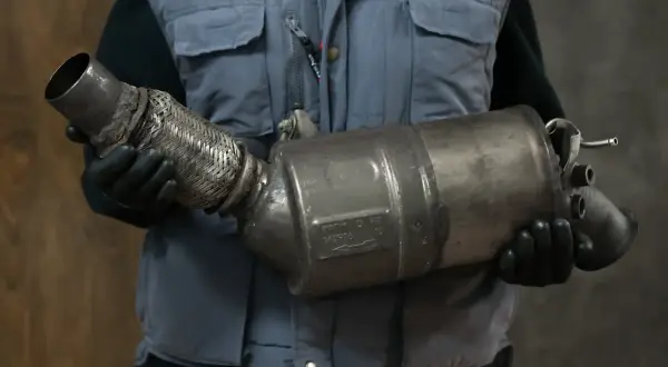 Mechanik w rękawiczkach trzyma zużyty element układu wydechowego, prawdopodobnie po problemach z wypalaniem DPF.