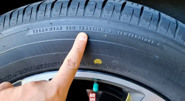 Palec wskazuje żółtą kropkę na oponie, obok napisu "TRACTION A".