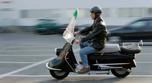 Mężczyzna w kasku i skórzanej kurtce jedzie czarnym motorowerem. To klasyczny pojazd, który wciąż budzi zachwyt.