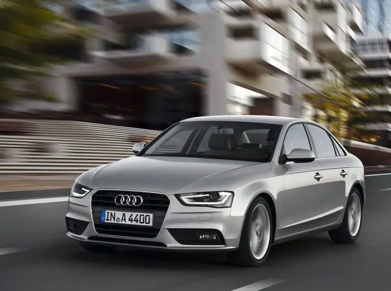 Srebrne Audi A4 B8 pędzi ulicą, rozmywając tło nowoczesnych budynków.