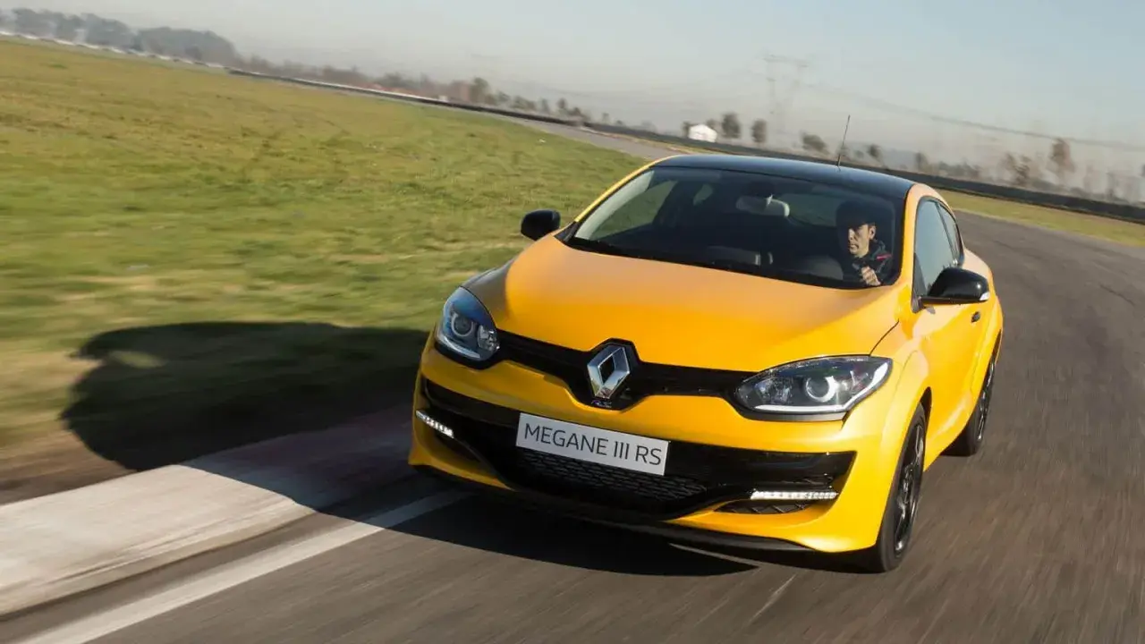 Żółty Megane RS na torze wyścigowym, kierowca w czapce z daszkiem za kierownicą.