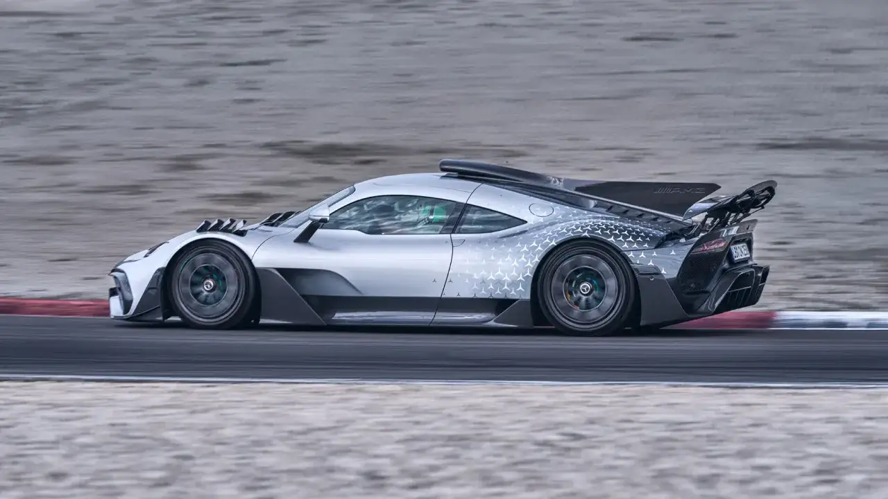 Srebrny Mercedes-AMG Project One pędzi po torze wyścigowym, jego aerodynamiczne linie i wzór gwiazd na karoserii podkreślają jego wyścigowe dziedzictwo.