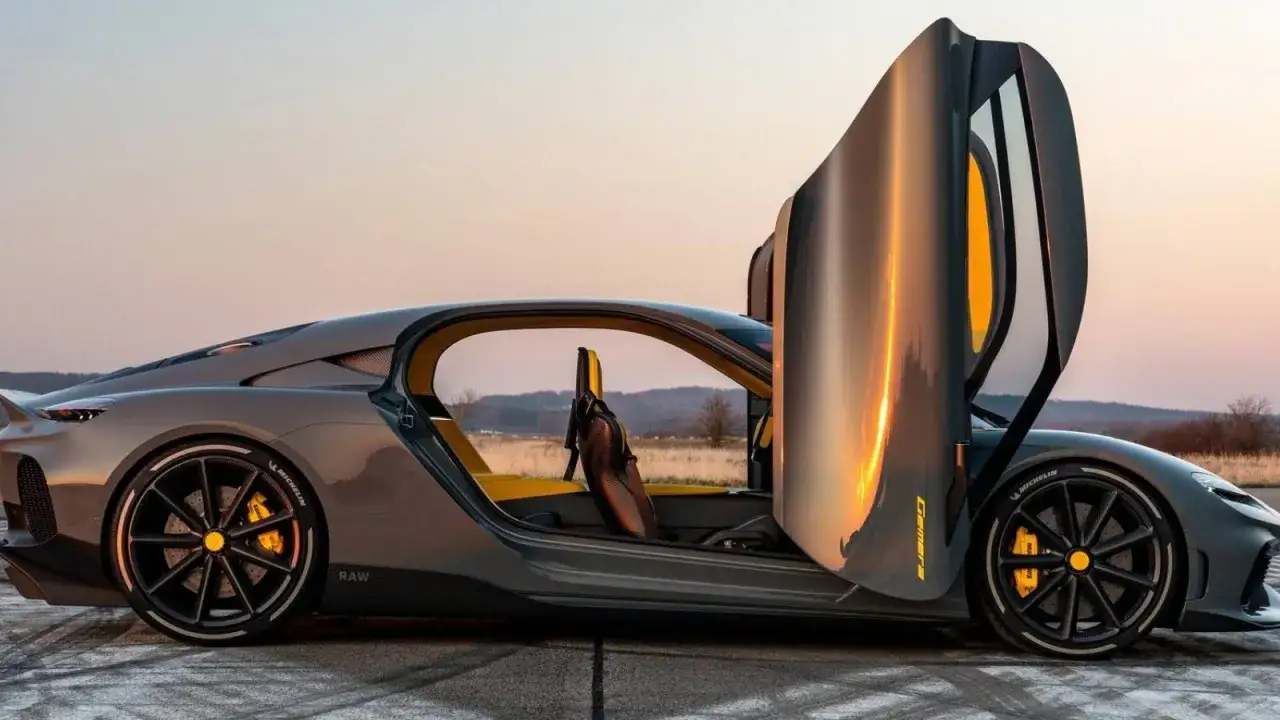 Szary Koenigsegg Gemera z otwartymi drzwiami, z żółtym wnętrzem, na tle zachodzącego słońca.