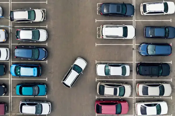 Widok z góry na parking, gdzie samochody zaparkowane są prostopadle. Widać różne kolory i modele aut.